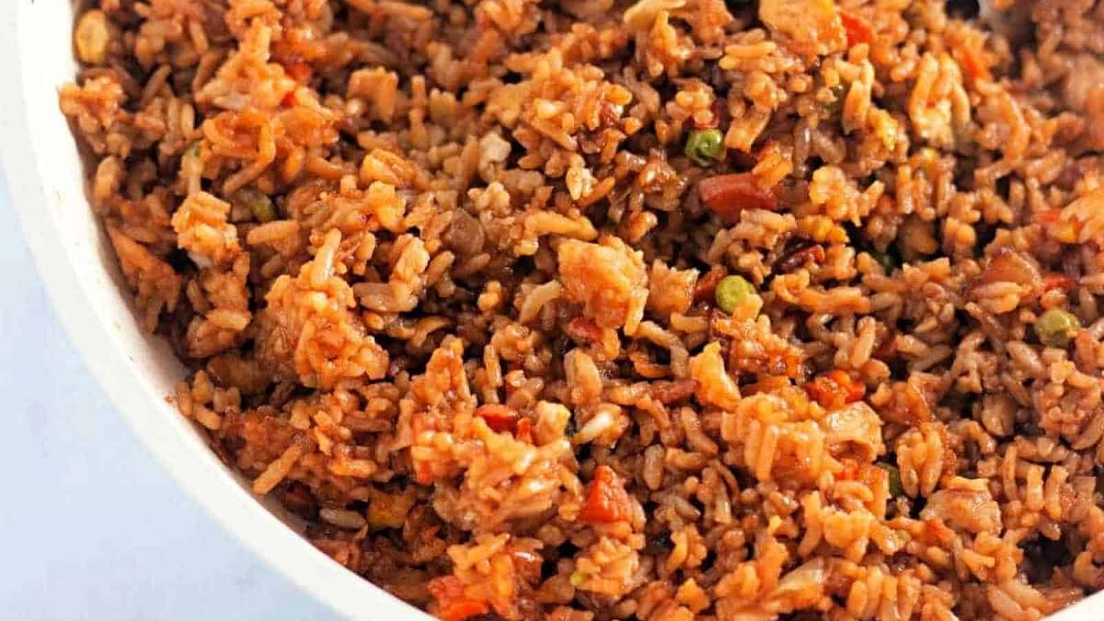 A close-up of a plate of fried rice mixed with vegetables, small pieces of meat, and a savory brown sauce.
