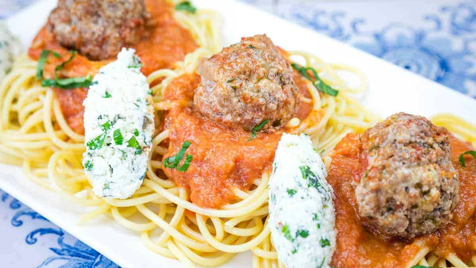 A white plate featuring spaghetti topped with ricotta meatballs and rich tomato sauce.