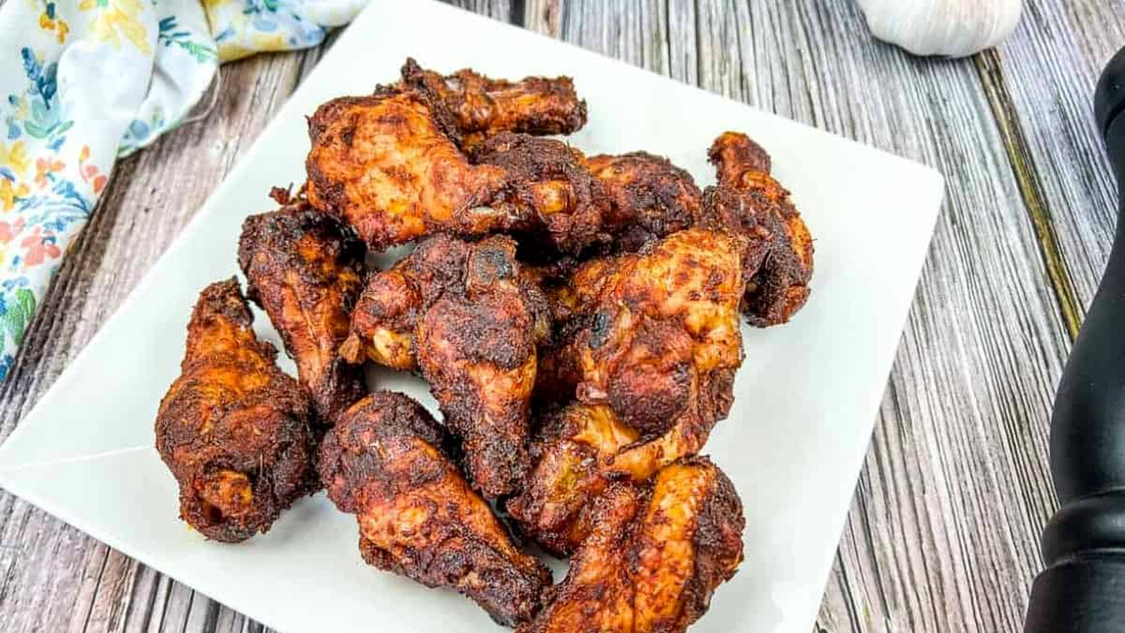 Smoked dry rubbed chicken wings on a white plate with garlic.