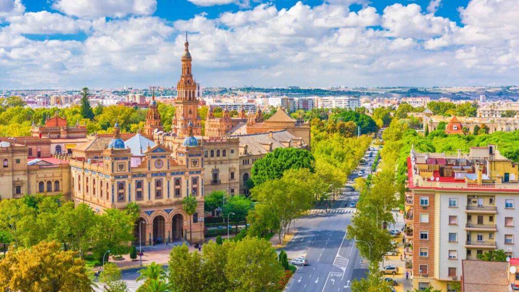 A wide view of Seville, Spain, featuring historic buildings, tree-lined streets, and a partly cloudy sky.