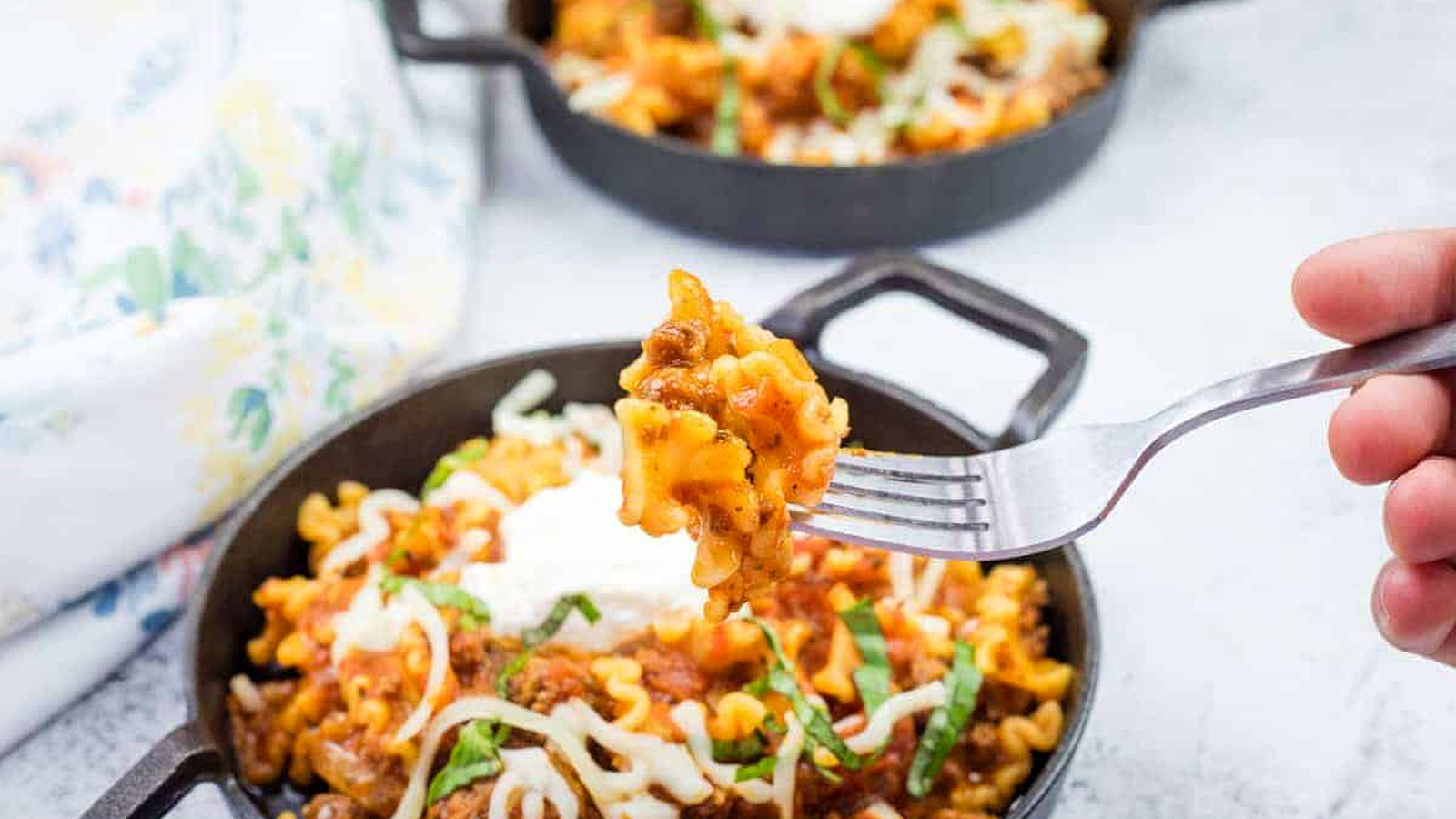 Two cast-iron skillets filled with skillet lasagna, topped with melted cheese.