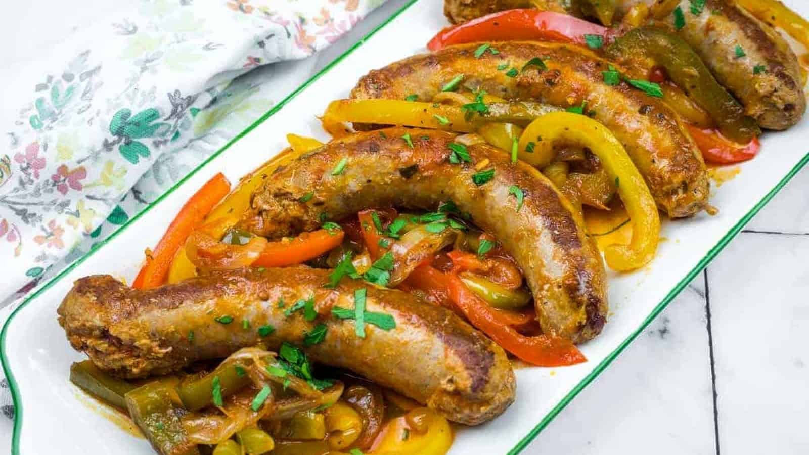 Five cooked Crock Pot Sausage and Peppers served on a white rectangular dish, garnished with chopped herbs.