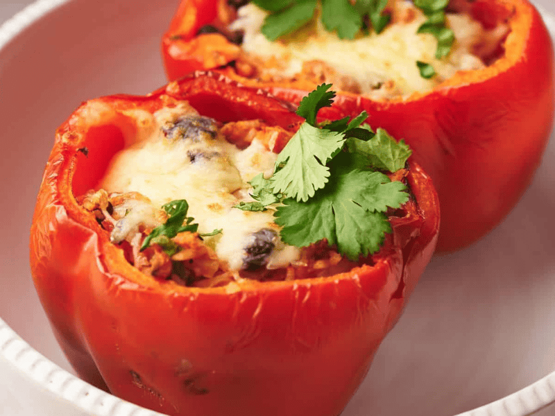 Two stuffed peppers in a bowl with melted cheese on top.