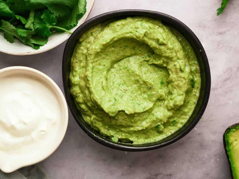 Avocado sauce in a bowl with it's ingredients surrounding it.