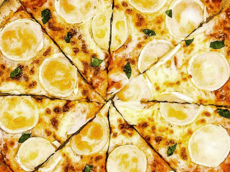 A pizza with cheese cut in half on a wooden board.