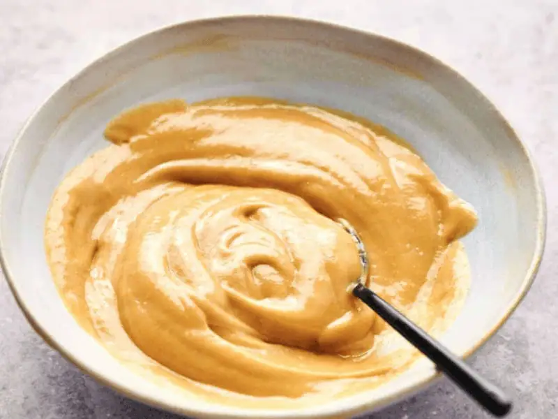 A bowl of smooth, creamy peanut butter with a hint of Chick-fil-A sauce and a spoon inside.