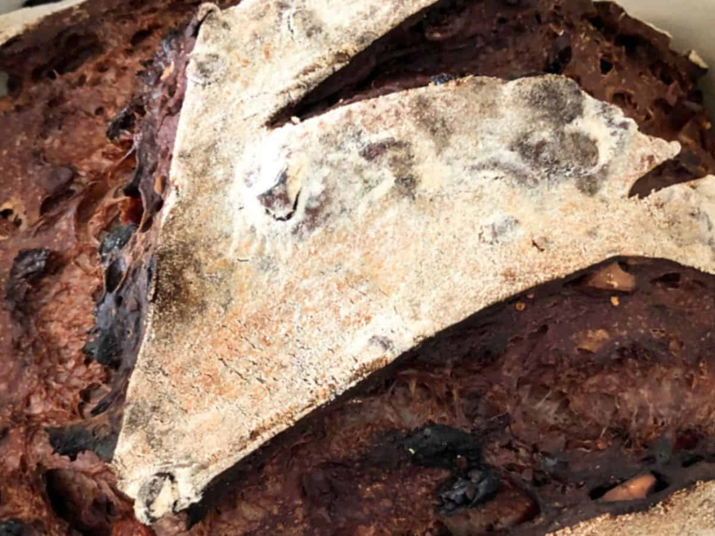 Close-up of a rustic, crusty loaf of bread with a dark, caramelized crust and visible scoring on the surface.