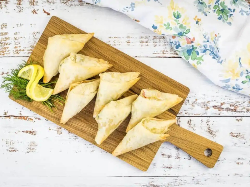 Crab Spanakopita triangles on a cutting board.