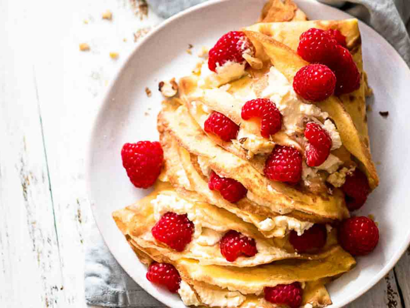 Plate of folded crepes with raspberries filling.