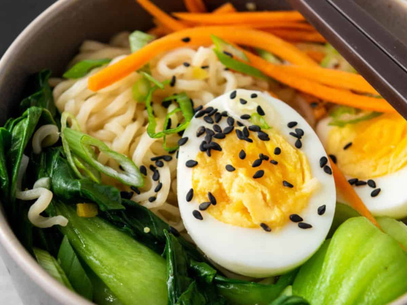 A bowl of ramen with soft-boiled egg, vegetables, and sesame seeds.