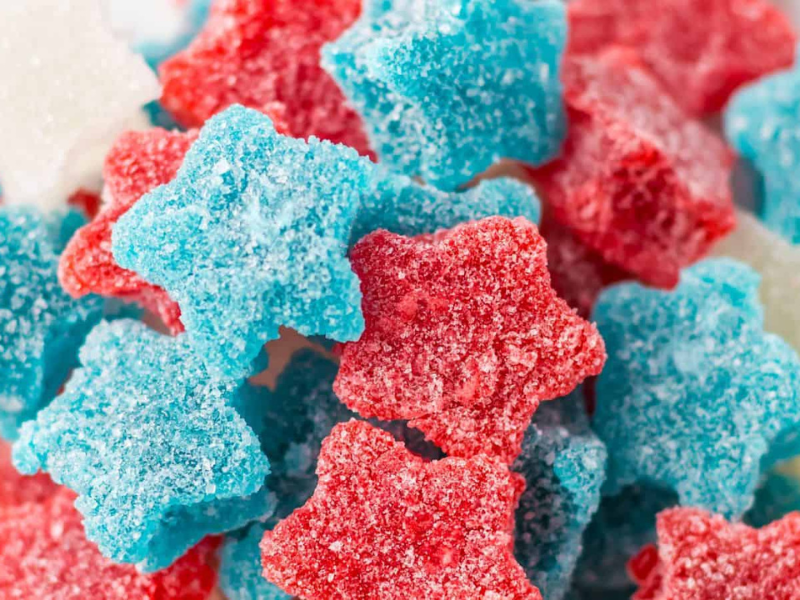 Close-up of star-shaped gummy candies in red, blue, and white, coated with sugar.
