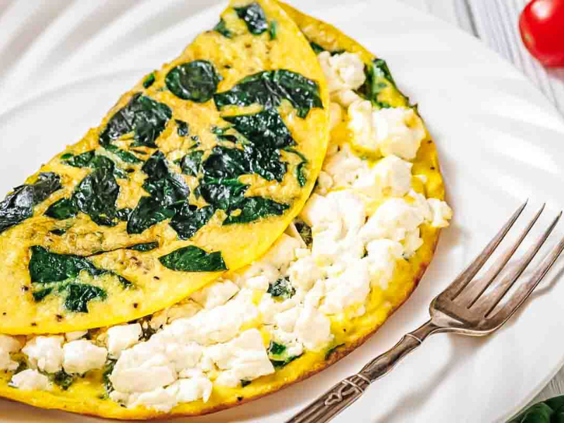 A spinach and feta cheese omelette folded on a white plate with a fork beside it.