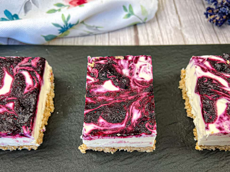 Three pieces of No-Bake Blueberry Cheesecake Bars on a black slate plate.