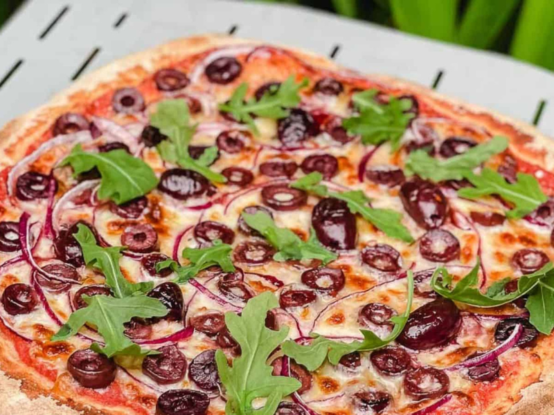 Cooked olive pizza on a pizza paddle.