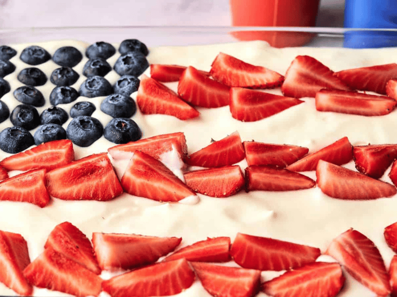 A dessert tray decorated like an American flag with blueberries in the top left corner and sliced strawberries arranged in rows on a white creamy base.