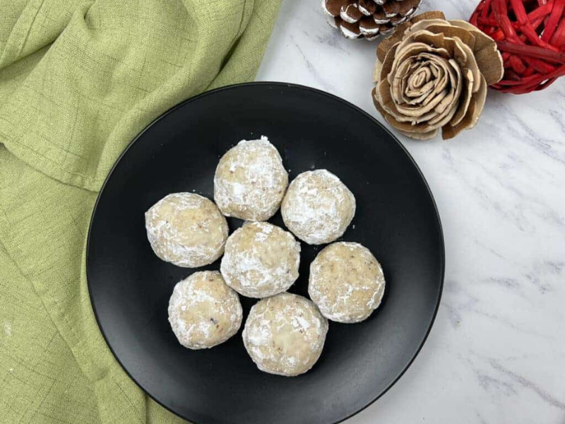 Top-down shot of seven pecan butter balls on a black plate.