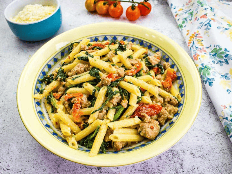 Broccoli Rabe and Sausage in a serving bowl with tomatoes in the background.