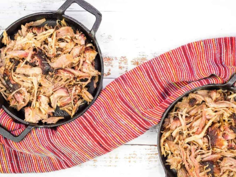 Two cast iron skillets with smoked pulled pork in them.