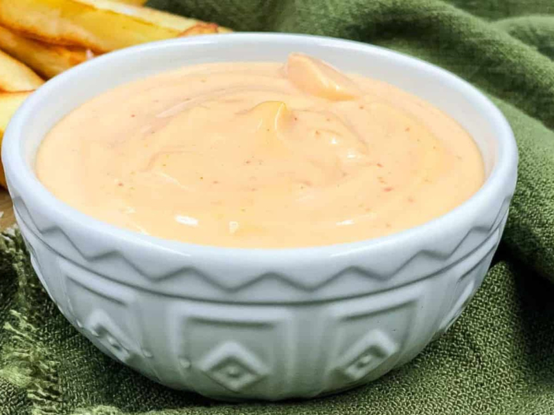 Sriracha aioli in a serving bowl and fries by the side of it.