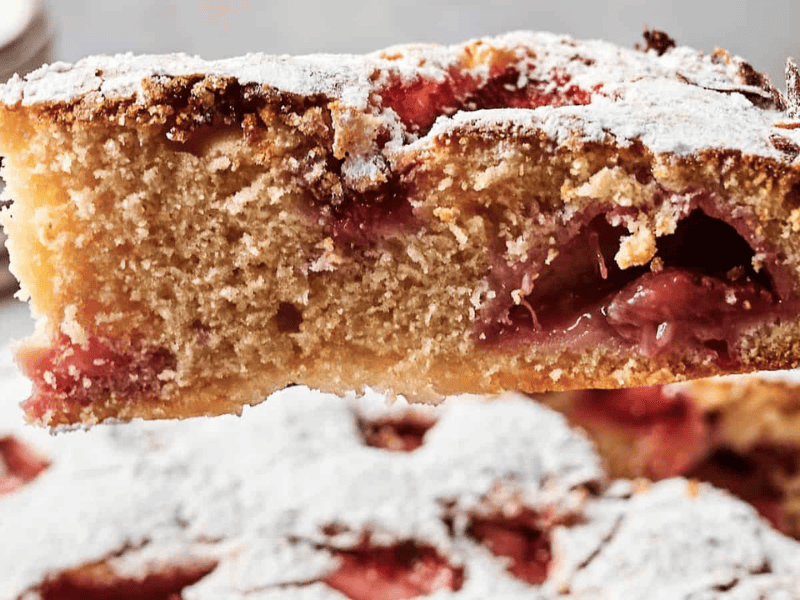 Close-up of a slice of strawberry cake dusted with powdered sugar, showing a fluffy texture and pieces of strawberries inside.
