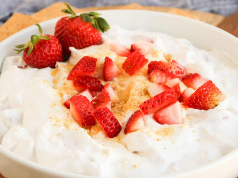 A white bowl filled with creamy dip topped with chopped fresh strawberries and a light sprinkle of crumbs.