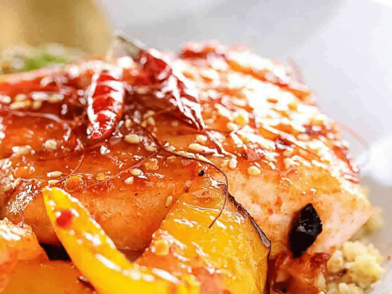 Close-up of a cooked salmon fillet topped with sesame seeds, dried red chilies, and sliced yellow bell peppers.