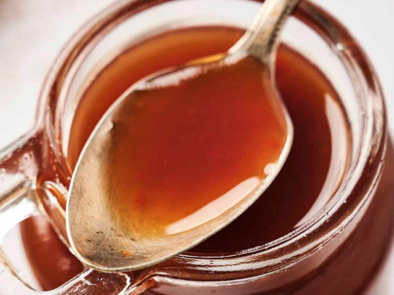 A spoon rests inside a glass jar filled with a thick, brown liquid.