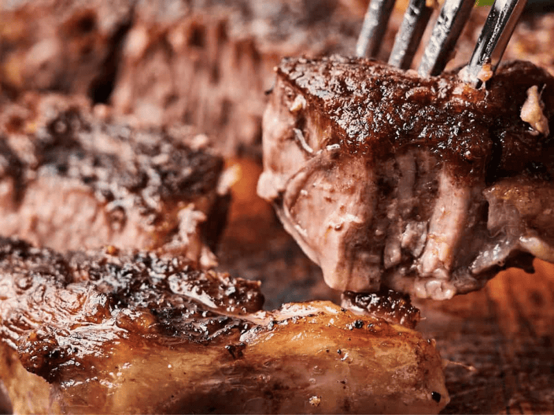 Close-up of cooked beef slices on a wooden board, with a fork holding one piece. The meat appears juicy with a seasoned crust.