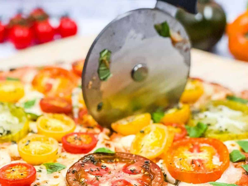 Someone slicing a pizza with a pizza cutter.