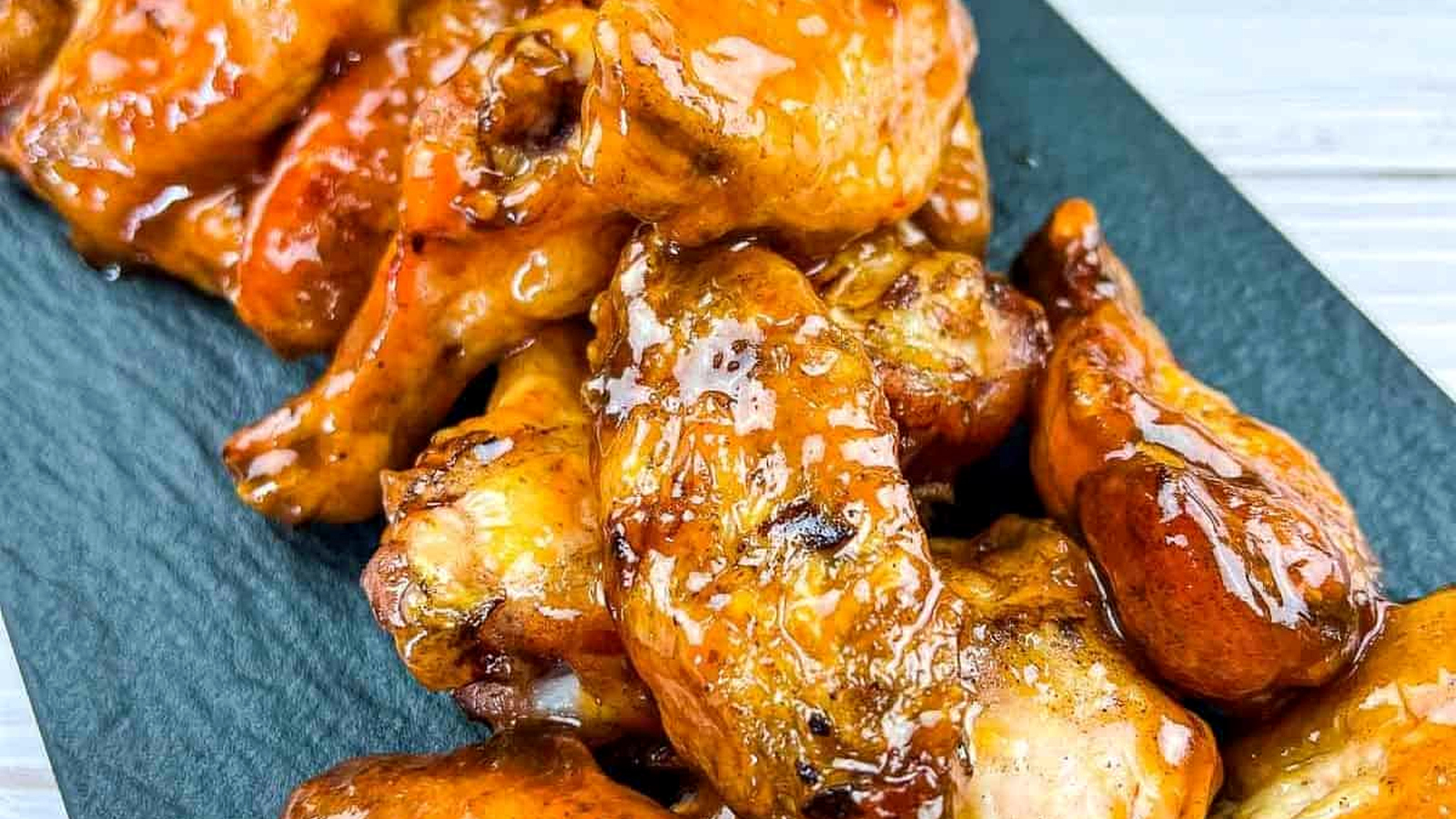 Smoked and glazed peach-chipotle chicken wings on a black plate.