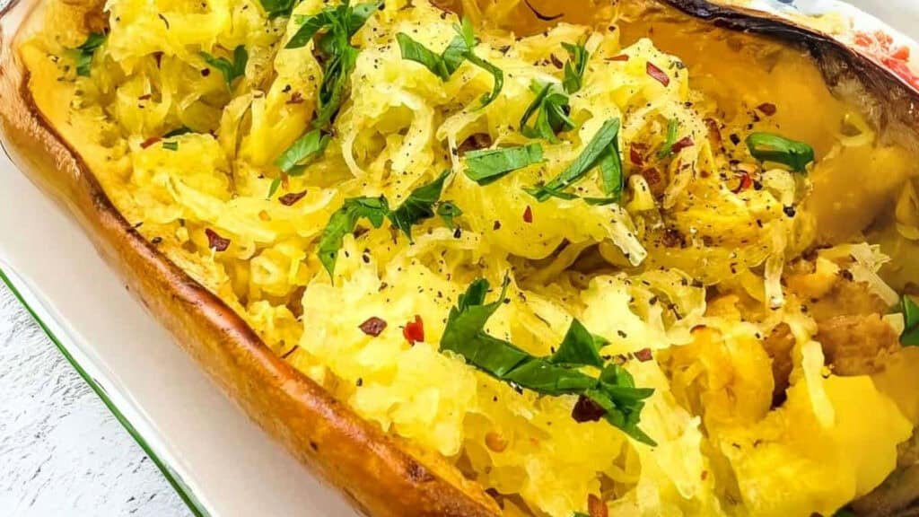 A baked spaghetti squash half filled with shredded squash, garnished with chopped parsley, red pepper flakes, and ground black pepper.