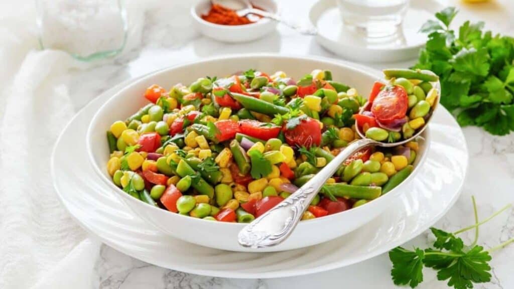 A white bowl filled with Southern succotash, with a serving spoon resting inside.