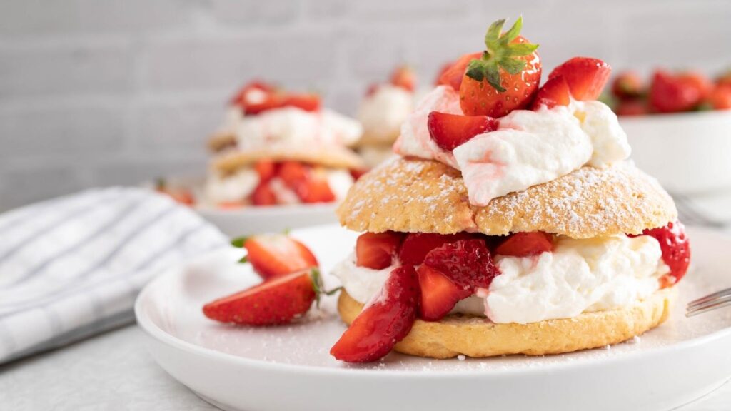 A plate with a strawberry shortcake layered with whipped cream and fresh strawberries, topped with a whole strawberry and dusted with powdered sugar.