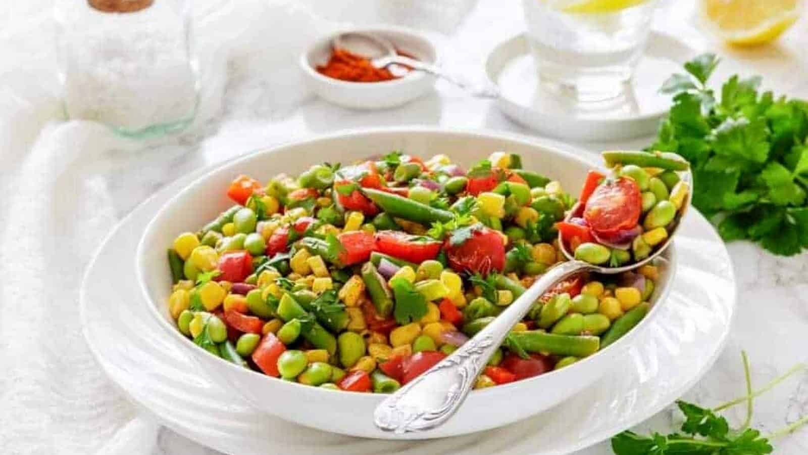 A white bowl filled with Southern Succotash with a serving spoon resting on the side.