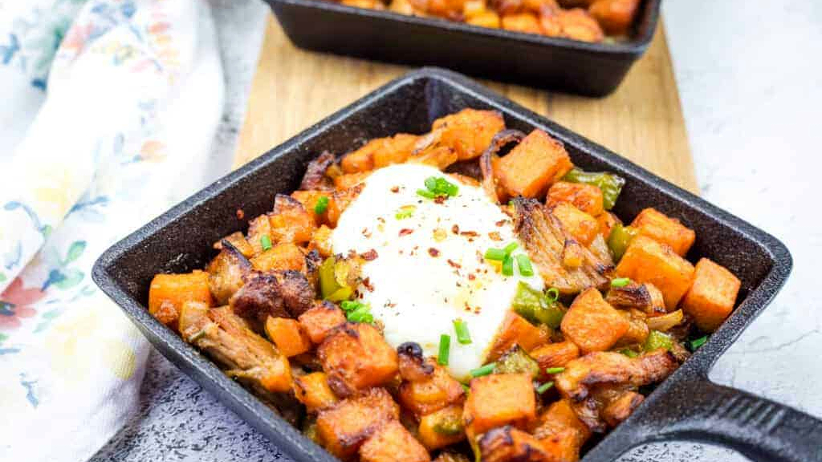 Cast iron skillet with sweet potato hash with pulled pork and garnished with chopped chives.