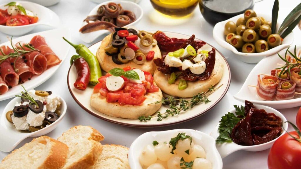 A variety of Italian appetizers including bruschetta, olives, cured meats, cheese, peppers, bread, and pickled vegetables arranged on a table&mdash;perfect for sharing during national movie night.