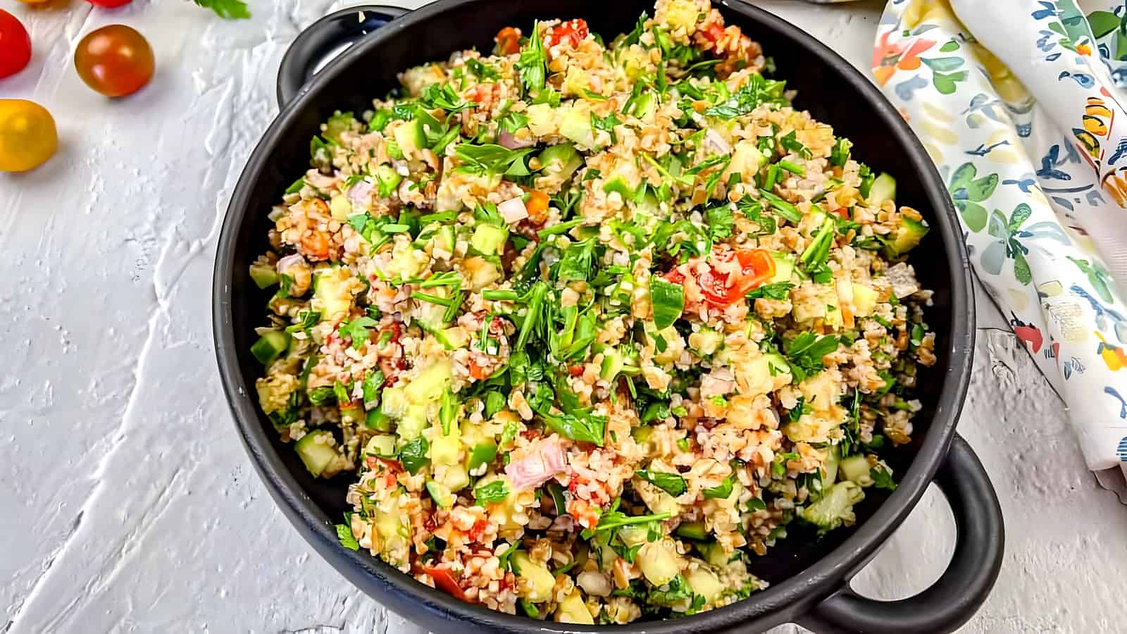 A black bowl filled with tabbouleh salad with smoked tomatoes.