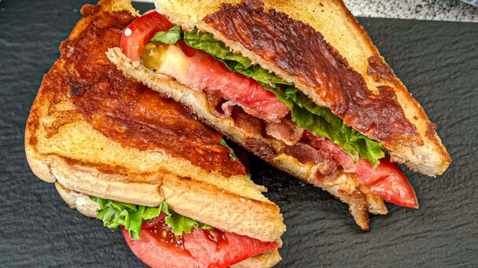 Two halves of Texas BLT on a black plate.