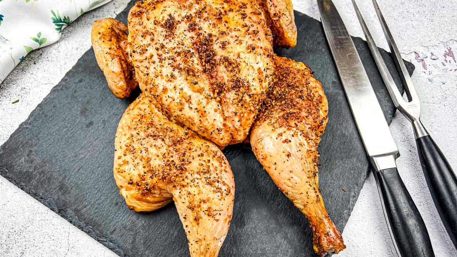 Roasted chicken on a slate board with carving knife and fork.