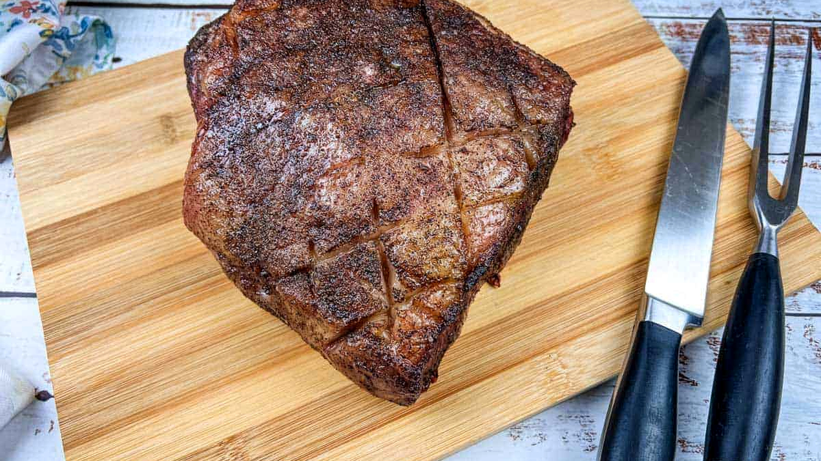 A piece of smoked New York strip roast meat on a cutting board next to a knife.