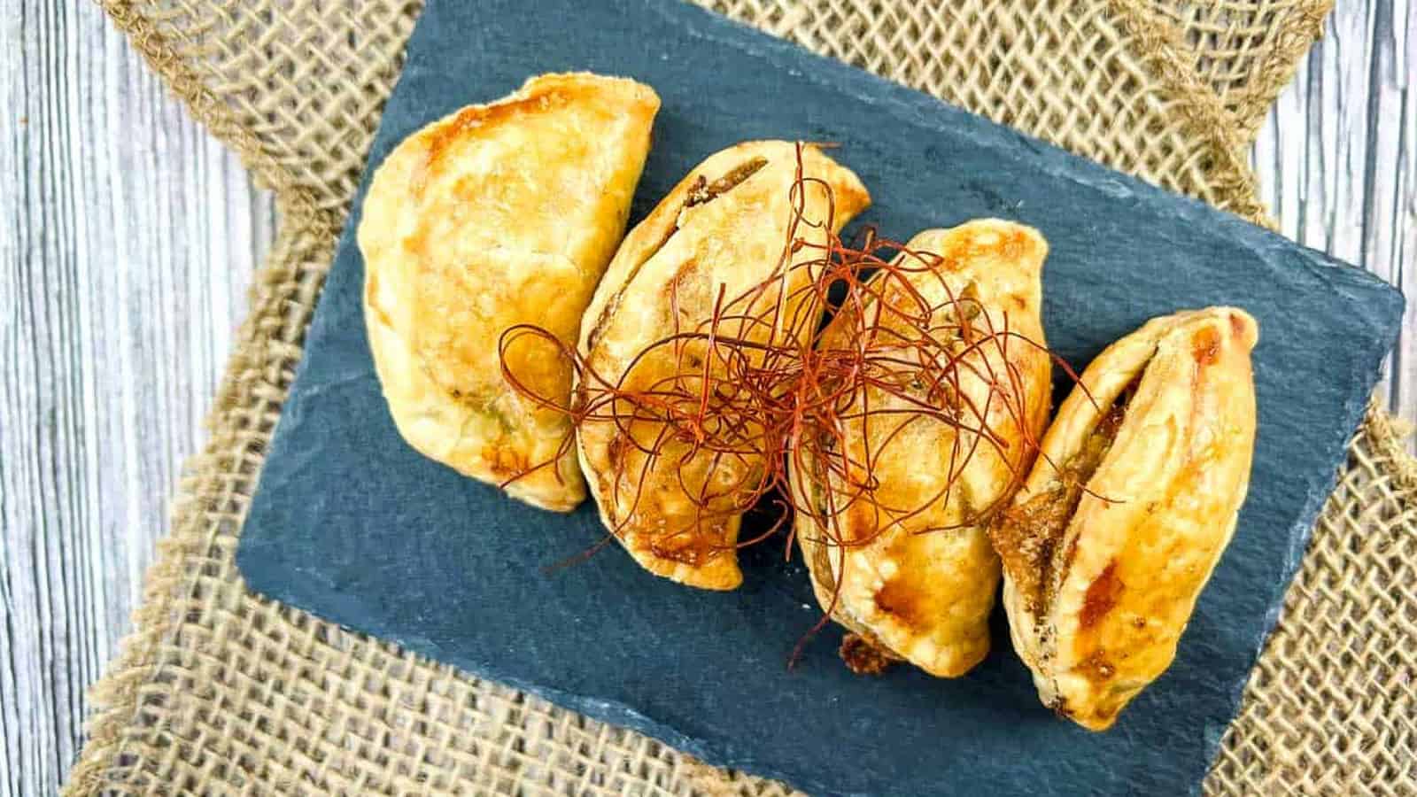 Four pieces of Air Fryer Beef Empanadas on a black rectangular slate.