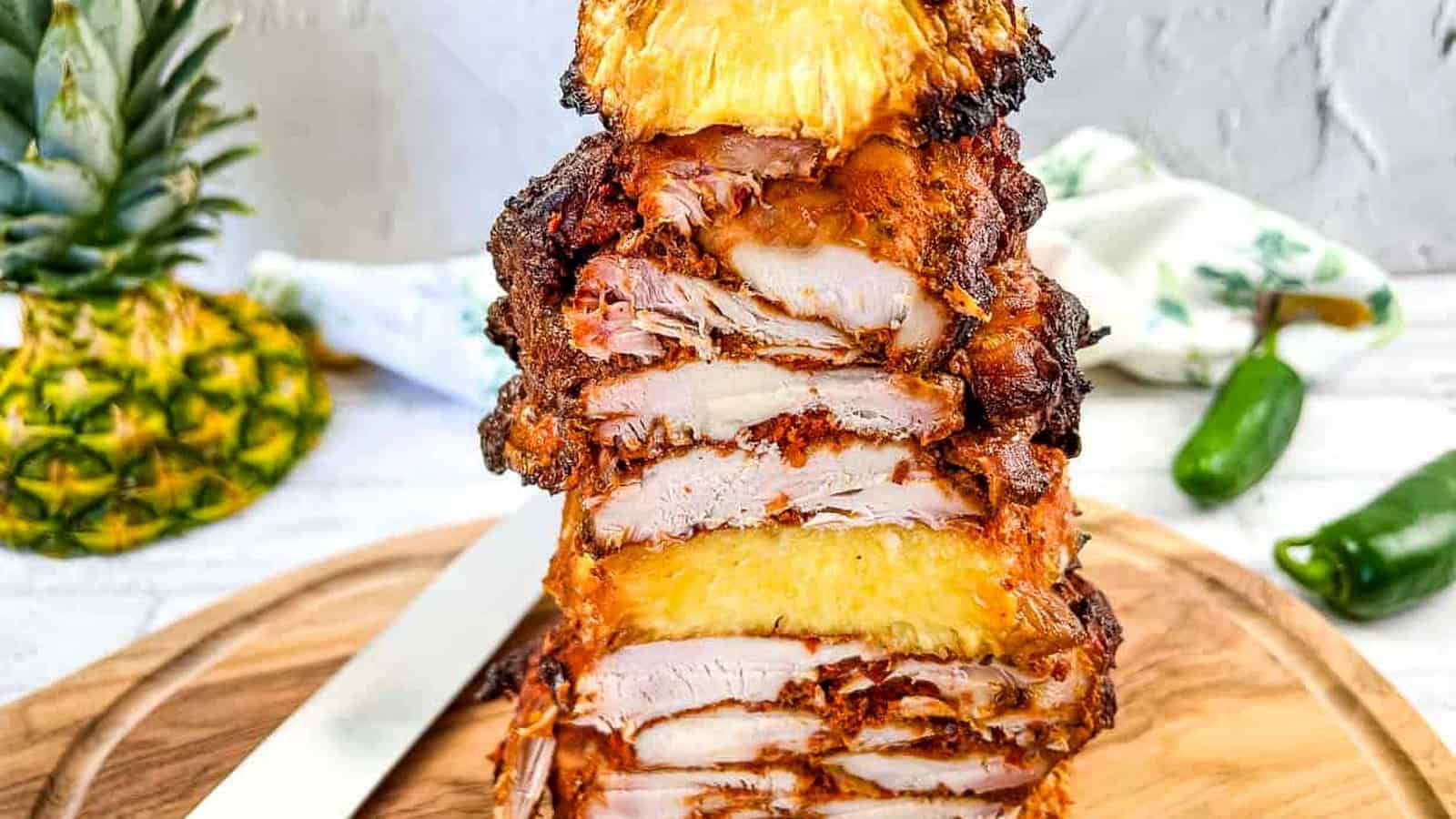 A stack of chicken and pineapple on a vertical skewer on a cutting board.