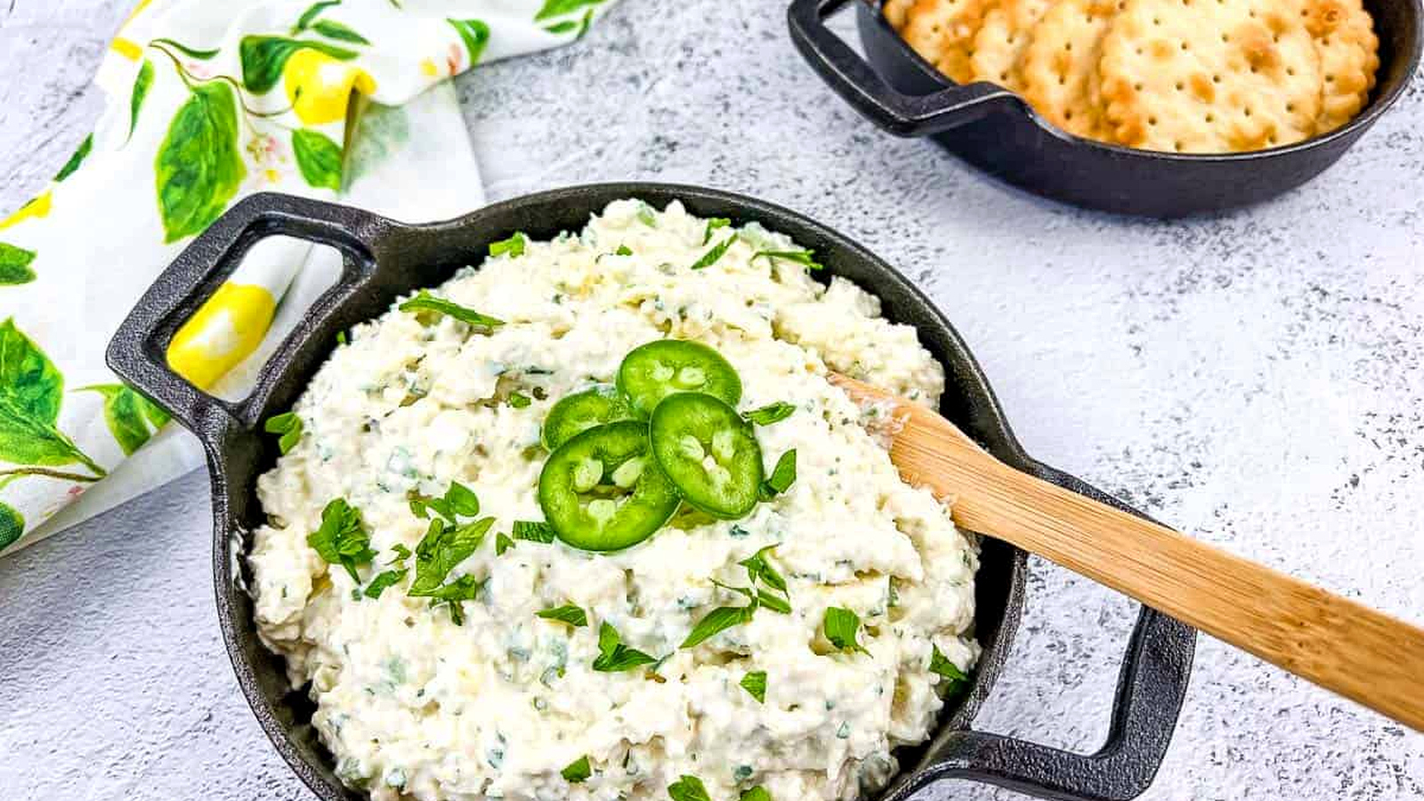 Artichoke Jalapeno Dip in a black bowl with crackers nearby.