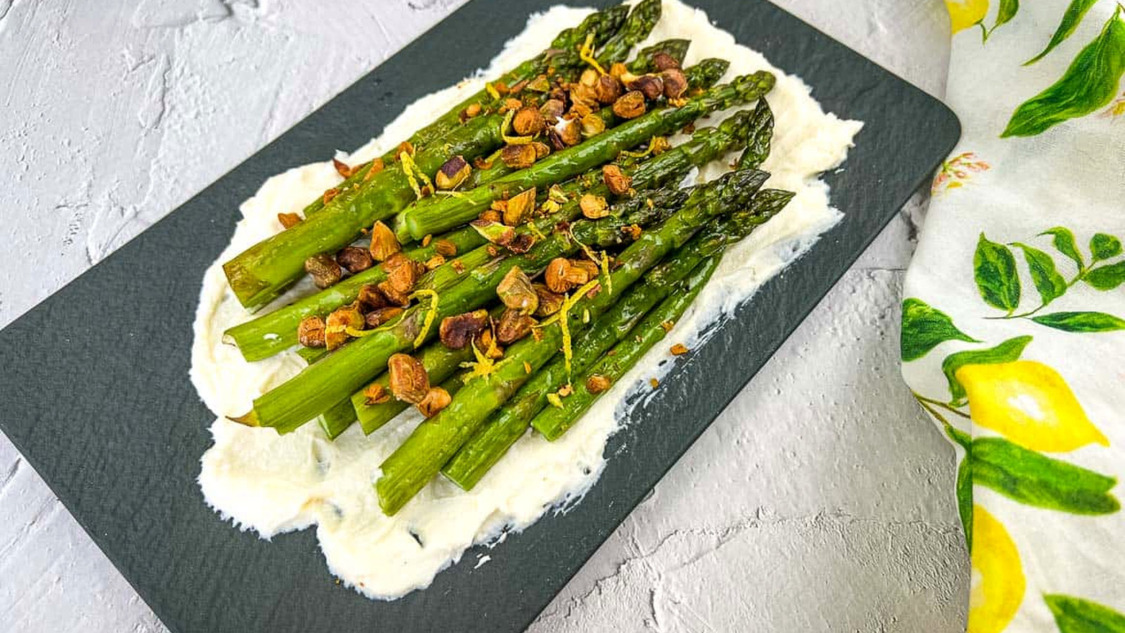 Oven-roasted asparagus on a bed of mascarpone, topped with toasted garlic, nuts, and lemon zest, served on a black slate platter.