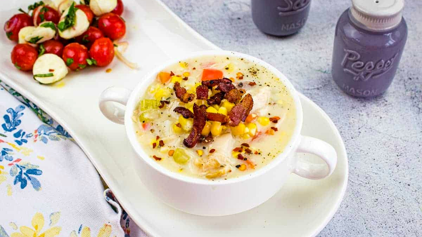 Chicken & Corn Chowder in a black bowl, topped with bacon, scallions, and red pepper flakes.