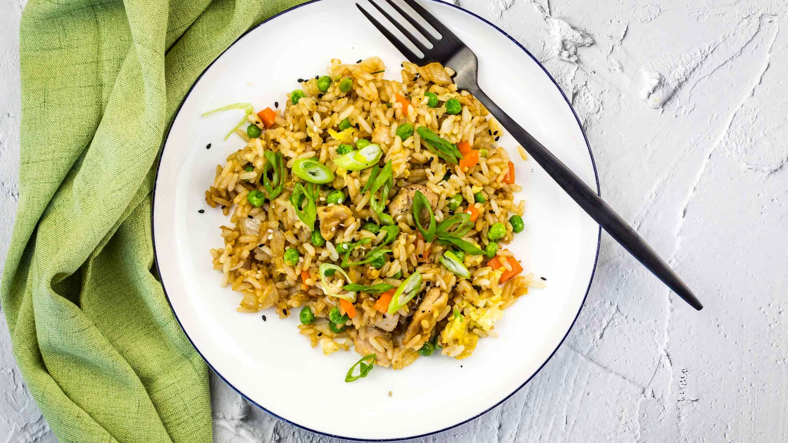 Chicken fried rice on a white plate with a green napkin.