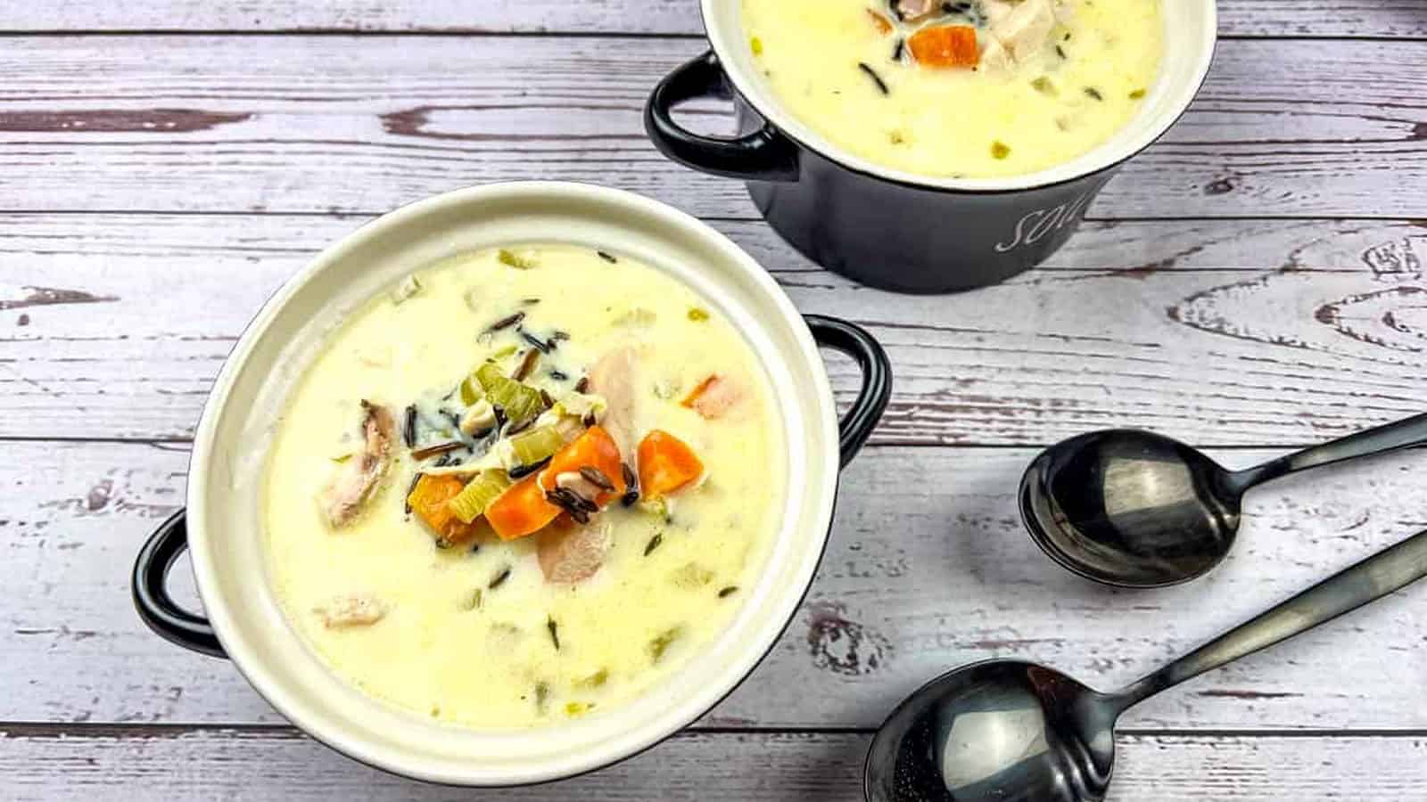 Two bowls of creamy chicken & wild rice soup on a wooden table.