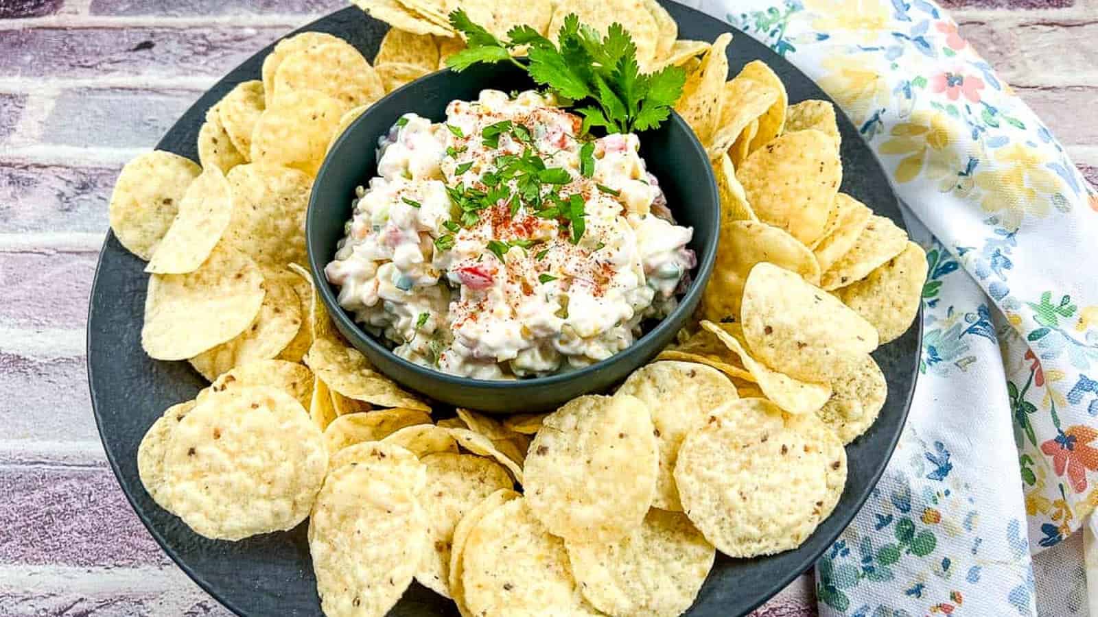 A bowl of Chilled Corn Dip with chips on a black plate.