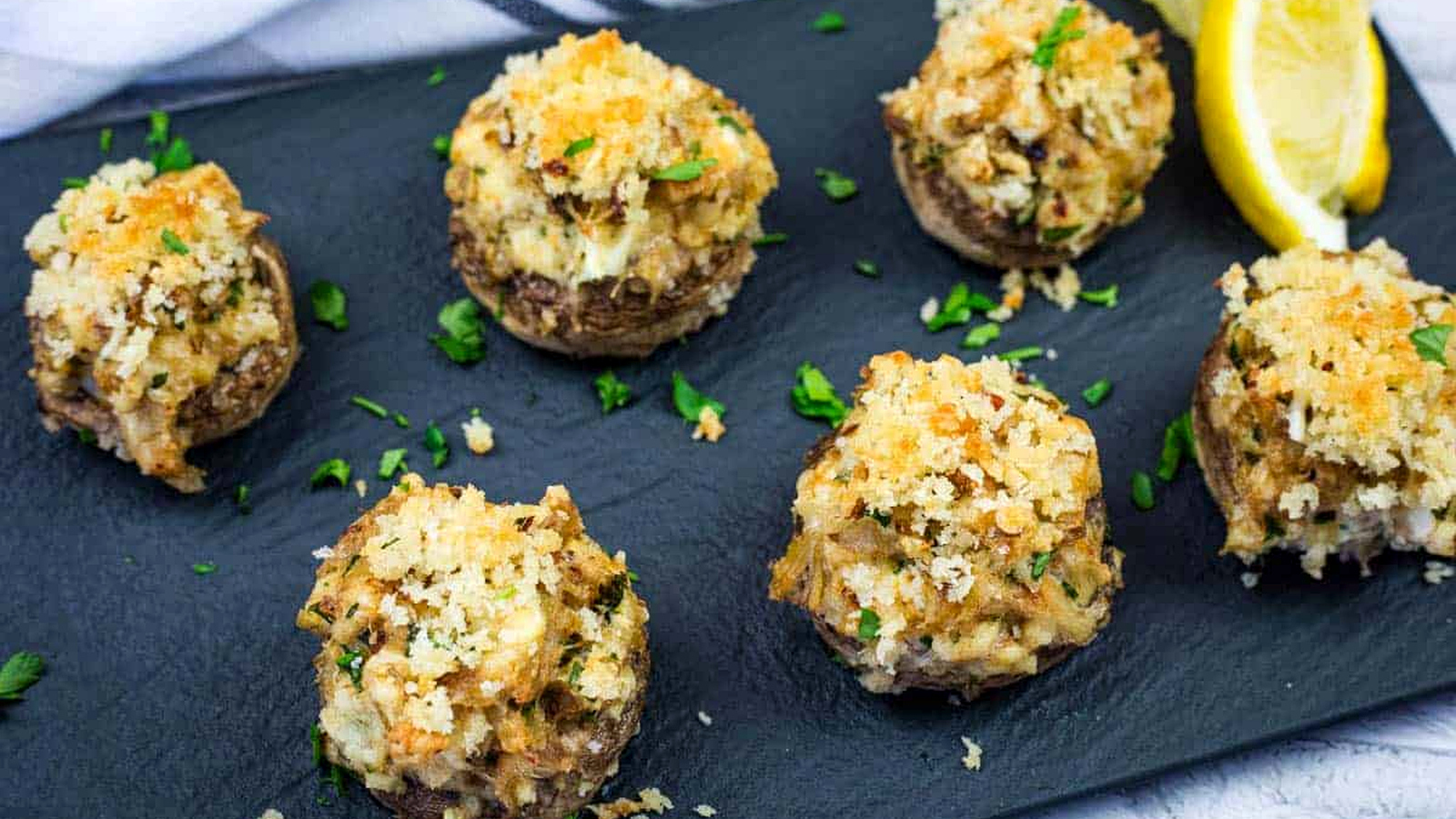 Close-up of Crab Stuffed Mushrooms garnished with chopped parsley on a slate plate.