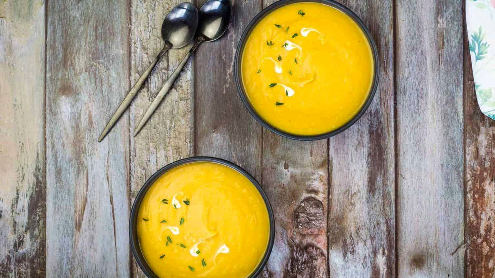 Two bowls of cream of butternut squash and sweet potato soup on a wooden table.